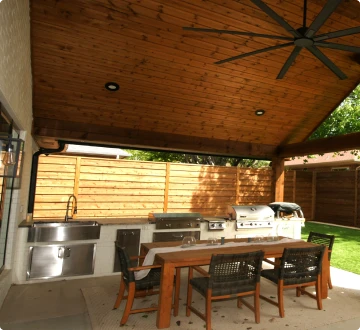 Outdoor kitchen and dining area with wood ceiling.